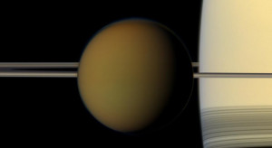 Barevný disk Saturnova největšího měsíce, Titanu, přechází před planetou a jejími prstenci. Vyfotografováno sondou Cassini (snímek v barevném provedení blízkém vnímání lidského oka. Zdroj: NASA/JPL-Caltech/Space Science Institute.